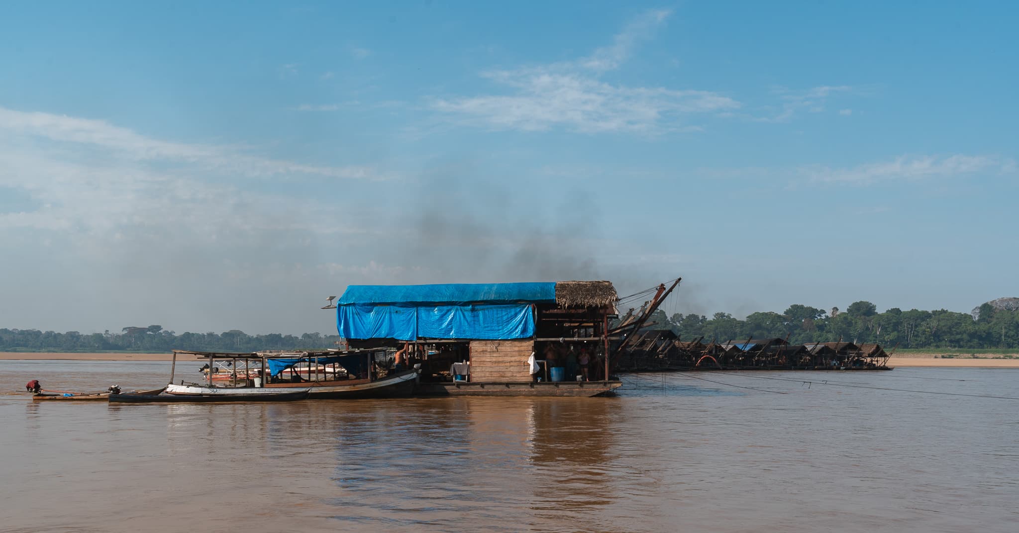 Une barge d'orpaillage bâchée de bleu, suivie de ses dragues, ancrée au milieu du fleuve amazonien