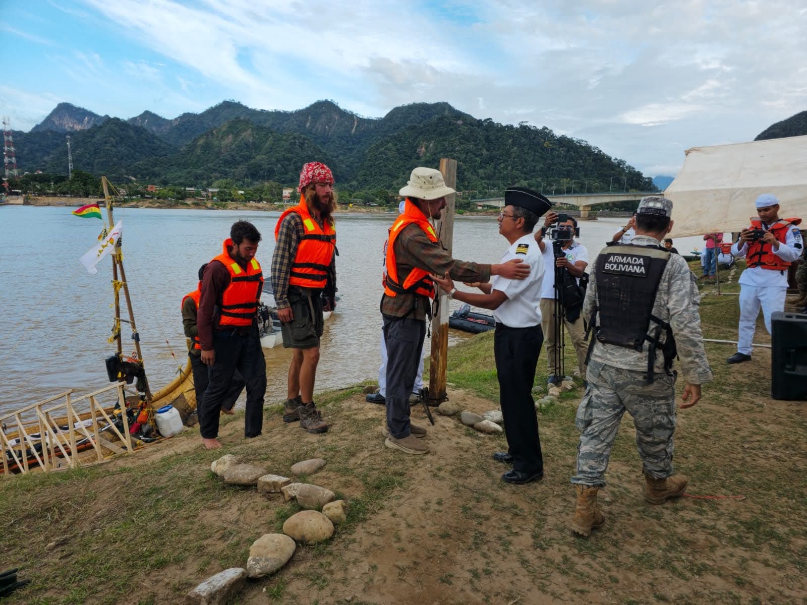 Cérémonie de départ : un officier de l'Armada Boliviana accueille l'équipage en gilets de sauvetage devant la balsa